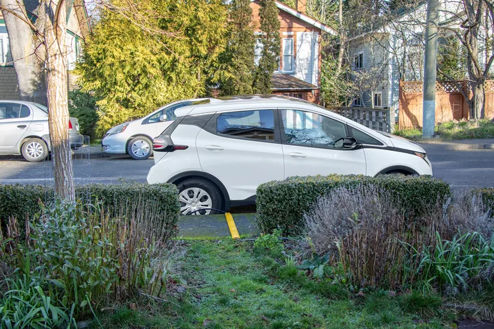 Electric vehicle beside a sidewalk with a covered charging cord